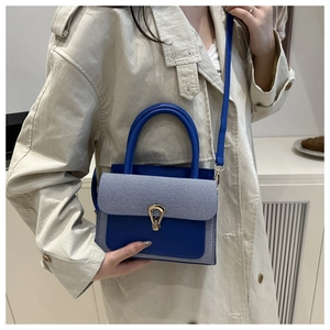 Detail of royal blue flap bag with striped fabric and gold clasp on a beige coat