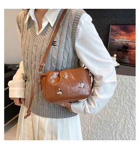 Detail of brown pleated cloud bag with silver butterfly charms and glossy PU leather