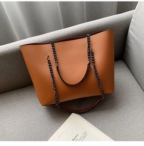 Detail of camel tote bag with double metal chain and leather straps on sofa