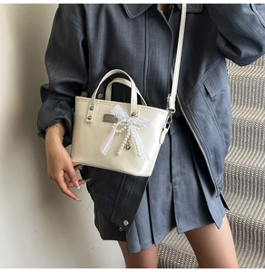 Close-up of cream leather handbag with delicate lace bow and pearl heart pendants