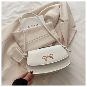 Detail of white leather shoulder bag with gold bow clasp and elegant knotted strap