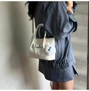 Detail of off-white pleated bucket bag featuring woven texture and fuzzy monster charm