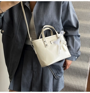 Detail of a creamy white mini bucket bag featuring a lace pearl bow and metal logo tag