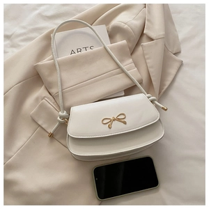 Close-up of white shoulder bag featuring a golden bow buckle and knotted strap detail