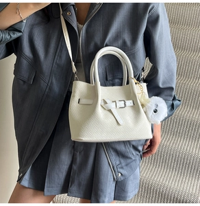 White woven tote bag with buckle straps and a cute plush cat charm on side