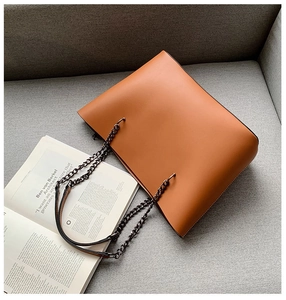 Close-up of a brown tote bag with metal chain strap and leather pad on a sofa