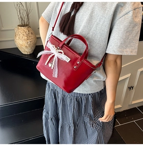 Detail of red patent leather mini bucket bag with lace bow and pearl charms worn by model