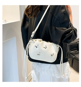 Close-up of white pleated crossbody bag with silver butterfly charms on a model