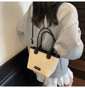 Détail du sac seau tissé avec bordure en cuir noir et bandoulière porté par un mannequin