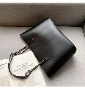 Detail of black leather tote bag with metal chain strap on minimalist background
