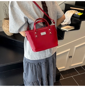 Detail of red patent leather bucket bag with silver studs and adjustable strap on a model