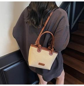 Détail du sac seau tissé beige avec bordure en cuir marron et détails dorés