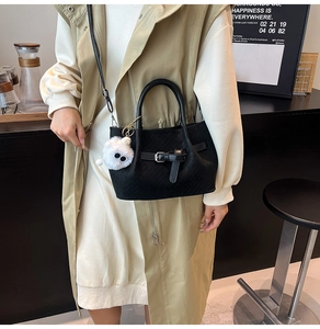 Detail of black woven bucket bag with metal buckle and a white monster plush charm