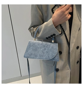 Detail of light blue denim texture trapezoid handbag with gold metal hardware and slim strap