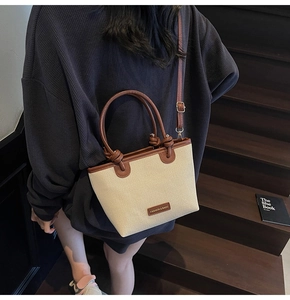 Détail d'un sac bandoulière tissé beige avec bordure en cuir marron porté par un mannequin