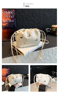 Detail of white pleated bucket bag with silver metal butterfly accents and knotted strap