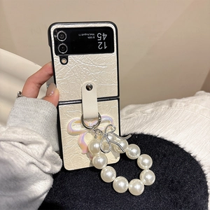 Close-up of cream leather phone case with large pearl ring and silver bow charm