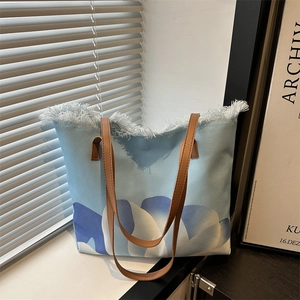 Bolso tote de lona con estampado de olas azules y asas de cuero sintético marrón bajo la luz
