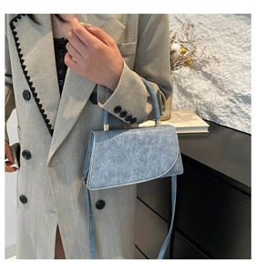 Detail of light blue textured small square bag with cylindrical handle and gold hardware