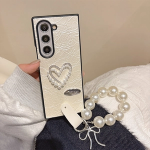 Detail of cream pleated leather phone case with pearl heart and silver bow charm