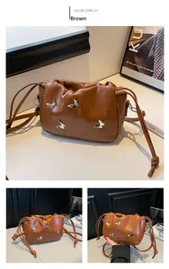 Detail of a brown ruched cloud bag featuring silver metal butterfly charms and vertical textures