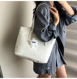 Detail of white tote bag featuring cartoon puppy embossing and a plush monster charm