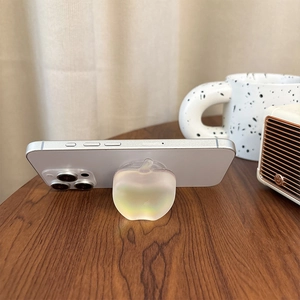 Iridescent apple-shaped phone grip on a silver smartphone over a wooden desk background
