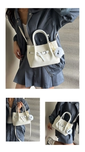 Close-up of white woven texture handbag with buckle detail and plush pendant