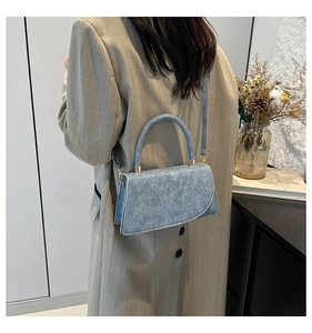 Detail of vintage denim blue crossbody bag worn by a model in a beige coat