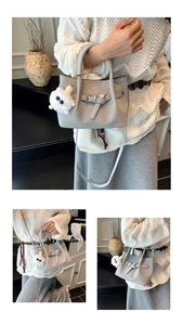 Detail of grey bucket bag with woven texture, leather buckle, and cute plush charm