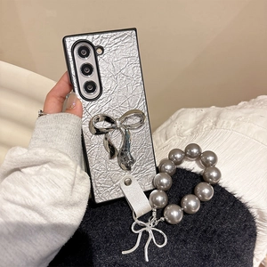 Detail of silver crinkled leather phone case with large metal bow and pearl bead strap