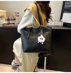 Detail of black tote bag with butterfly embossing and plush ram keychain accessory