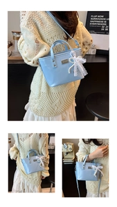 Detail of light blue bucket bag with pearl and lace bow charms on a leather strap