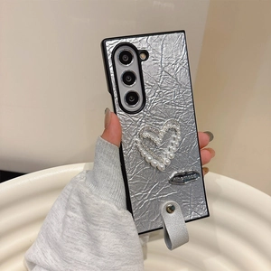 Close-up of silver wrinkled leather texture with pearl and rhinestone heart on phone case
