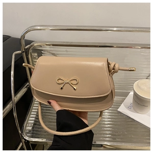 Detail of apricot saddle bag with golden bow hardware and elegant thin shoulder strap