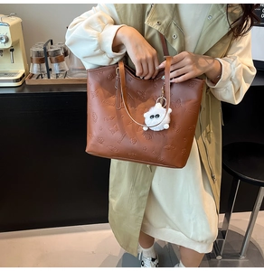 Close-up of brown embossed leather tote bag with a white plush monster pendant