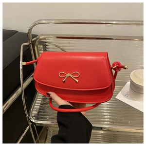 Detail of red glossy shoulder bag with golden bow hardware on a minimalist glass shelf