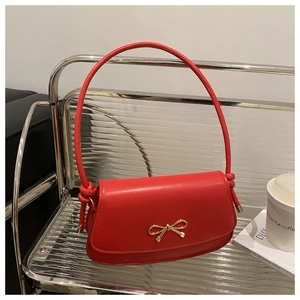 Close-up of red leather handbag featuring a golden bow buckle and knotted strap detail