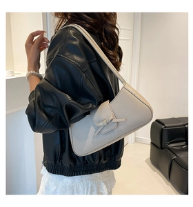Detalle del bolso baguette beige con lazo y textura de cuero suave sobre el hombro