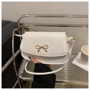 Detail shot of a white matte saddle bag featuring a decorative golden bow metal buckle