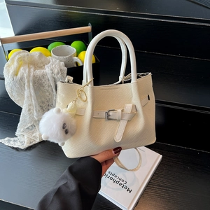 Elegant cream pleated bucket bag with silver buckle and plush pompom charm on black steps