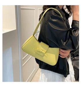 Detail of light yellow baguette bag with bow accent on model in stylish black jacket