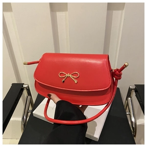 Close-up of vibrant red leather handbag featuring a signature gold bow metal clasp detail