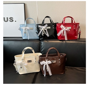 Close-up of patent leather bucket bags with lace bows and pearl charms in five colors