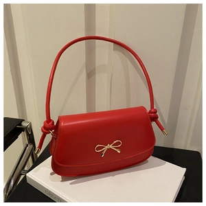Detail of red leather crossbody bag featuring an elegant golden bow buckle on the cover