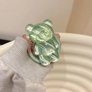 Close-up of a translucent green bear phone grip with iridescent finish and Good Luck text