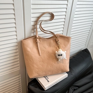 Large vintage beige tote bag with floral embossing and plush charm on leather sofa