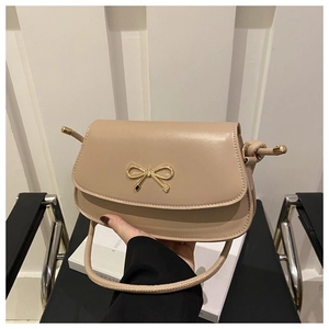 Detailed view of cream leather handbag with gold bow metal buckle and flap closure