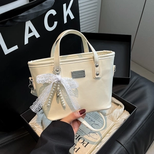 Chic cream bucket bag with lace bow and pearl charm shown in a stylish hand-held pose