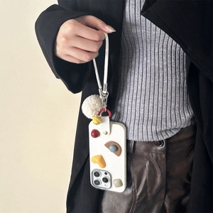 Detail of cream silicone phone case with colorful 3D charms and fluffy white pompom strap